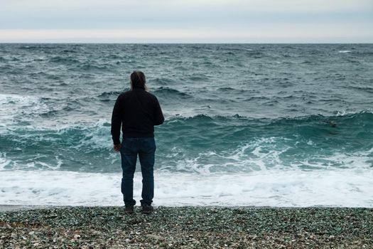 a man stands by the sea on a cloudy day and looks at the big waves.