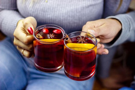 Hot mulled wine in male and female hands, spices. Sweet home concept