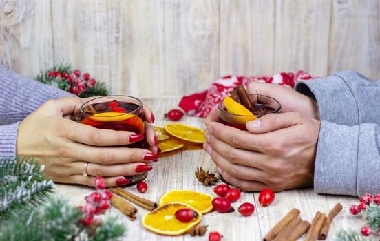 Hot mulled wine in female hands, spices on weathered wooden table. Sweet-home concept