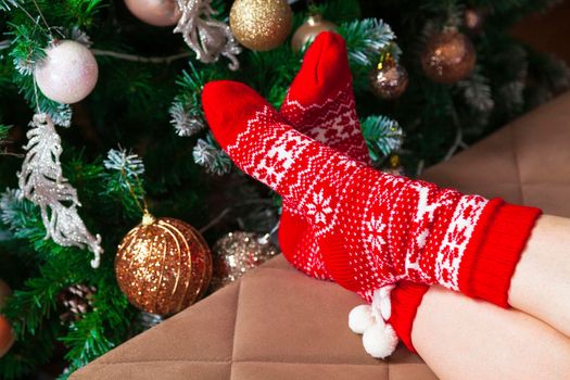 Female feet in red knitted socks and decorated Christmas tree