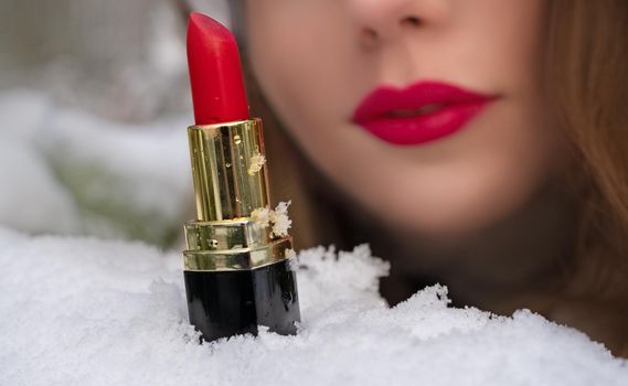 lipstick on the snow against the background of a young woman's face out of focus