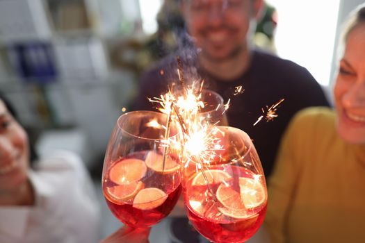 Group of people is holding glasses with cocktail with alcohol and sparklers. Christmas party concept