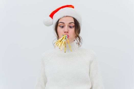 Young woman in santa hat blowing festive pipe isolated on white background