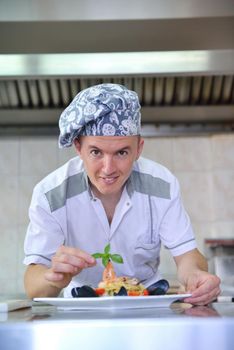 Handsome chef dressed in white uniform decorating pasta salad and seafood fish in modern kitchen