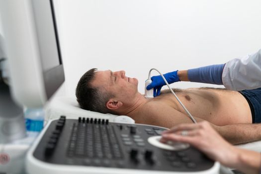 Doctor using ultrasound machine to scan heart of a male patient. Cardiologist makes a patient an echocardiographic test in a clinic. Patient under ultrasound examination in the hospital. Cardiovascular tests.