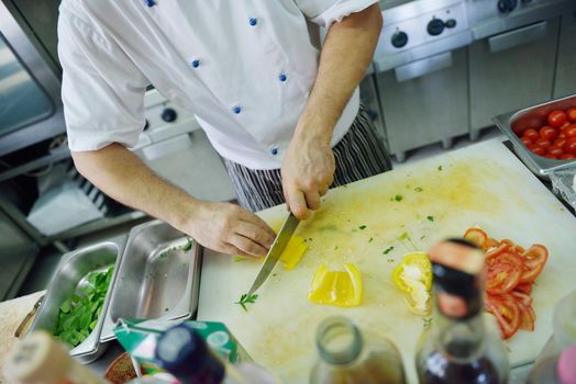 Handsome chef dressed in white uniform decorating pasta salad and seafood fish in modern kitchen