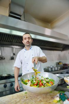 Handsome chef dressed in white uniform decorating pasta salad and seafood fish in modern kitchen