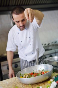 Handsome chef dressed in white uniform decorating pasta salad and seafood fish in modern kitchen