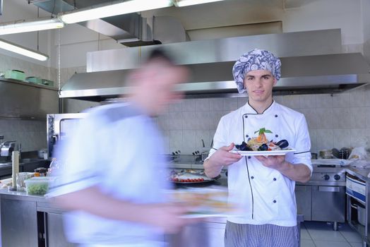 Handsome chef dressed in white uniform decorating pasta salad and seafood fish in modern kitchen