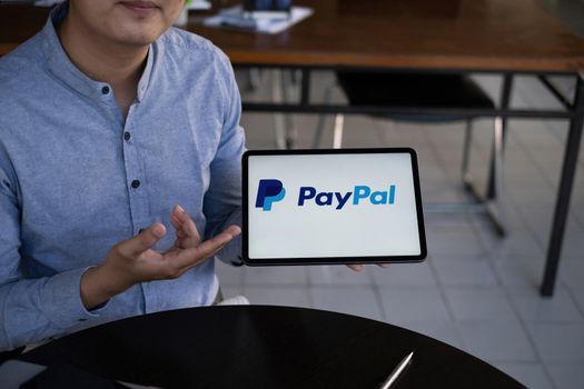 CHIANG MAI, THAILAND - 29 NOV 2021 : Man using Ipad with paypal logo on screen. PayPal is a worldwide online payment system and one of the most popular ways of making payment on the Internet.