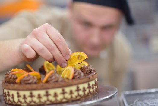 Closeup of a concentrated male pastry chef decorating dessert cake food in the kitchen