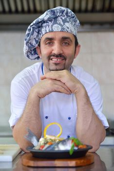 Handsome chef dressed in white uniform decorating pasta salad and seafood fish in modern kitchen