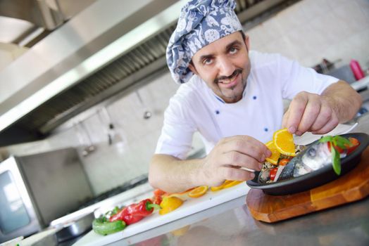 Handsome chef dressed in white uniform decorating pasta salad and seafood fish in modern kitchen