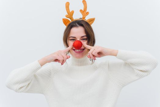 Photo of an overjoyed funny lady in a christmas deer costume and a white sweater with a red bauble and a white background.