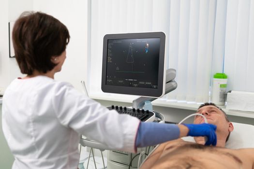 Doctor using ultrasound machine to scan heart of a male patient. Cardiologist makes a patient an echocardiographic test in a clinic. Patient under ultrasound examination in the hospital. Cardiovascular tests.