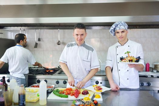 Handsome chef dressed in white uniform decorating pasta salad and seafood fish in modern kitchen