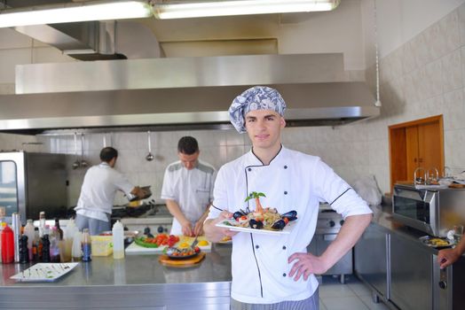 Handsome chef dressed in white uniform decorating pasta salad and seafood fish in modern kitchen