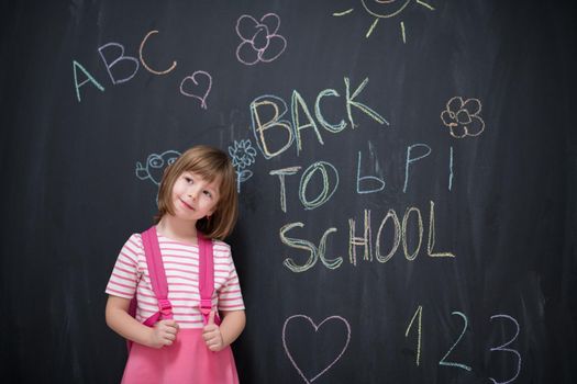 Happy school girl child with backpack writing  back to school on black chalkboard