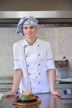 Handsome chef dressed in white uniform decorating pasta salad and seafood fish in modern kitchen