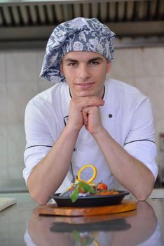 Handsome chef dressed in white uniform decorating pasta salad and seafood fish in modern kitchen