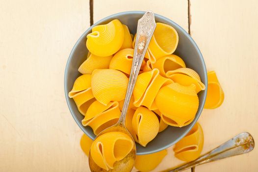 raw Italian snail lumaconi pasta on a blue bowl over rustic table macro