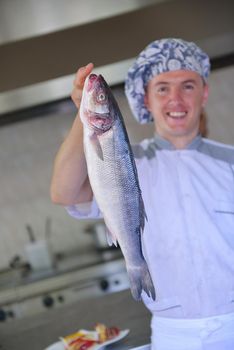 Handsome chef dressed in white uniform decorating pasta salad and seafood fish in modern kitchen