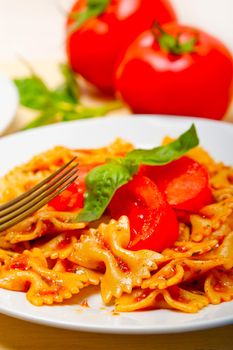 Italian pasta farfalle butterfly bow-tie with tomato basil sauce over white rustic wood table