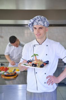 Handsome chef dressed in white uniform decorating pasta salad and seafood fish in modern kitchen