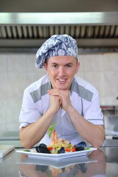 Handsome chef dressed in white uniform decorating pasta salad and seafood fish in modern kitchen