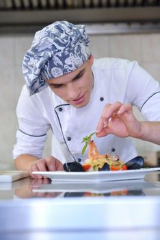 Handsome chef dressed in white uniform decorating pasta salad and seafood fish in modern kitchen