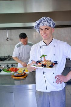 Handsome chef dressed in white uniform decorating pasta salad and seafood fish in modern kitchen