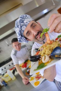 Handsome chef dressed in white uniform decorating pasta salad and seafood fish in modern kitchen