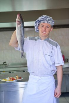 Handsome chef dressed in white uniform decorating pasta salad and seafood fish in modern kitchen