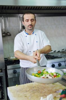 Handsome chef dressed in white uniform decorating pasta salad and seafood fish in modern kitchen