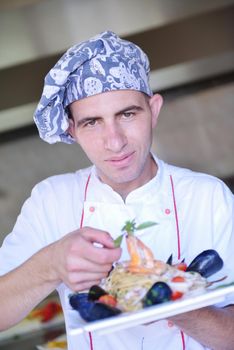 Handsome chef dressed in white uniform decorating pasta salad and seafood fish in modern kitchen