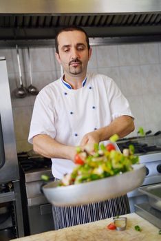 Handsome chef dressed in white uniform decorating pasta salad and seafood fish in modern kitchen