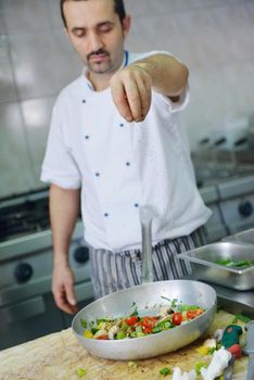 Handsome chef dressed in white uniform decorating pasta salad and seafood fish in modern kitchen