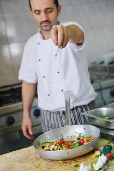 Handsome chef dressed in white uniform decorating pasta salad and seafood fish in modern kitchen