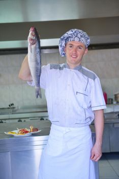 Handsome chef dressed in white uniform decorating pasta salad and seafood fish in modern kitchen