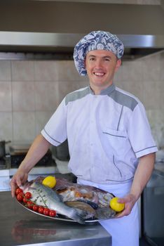 Handsome chef dressed in white uniform decorating pasta salad and seafood fish in modern kitchen