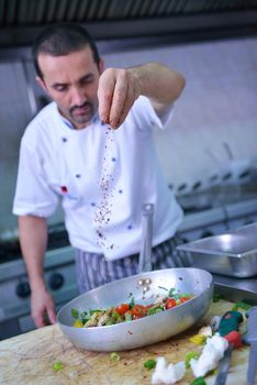 Handsome chef dressed in white uniform decorating pasta salad and seafood fish in modern kitchen