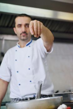 Handsome chef dressed in white uniform decorating pasta salad and seafood fish in modern kitchen