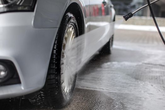 Detail on silver car front wheel being washed with jet water spray in carwash.