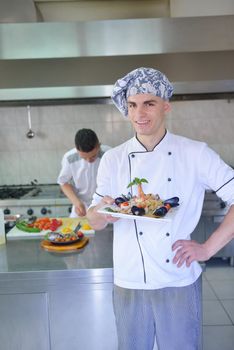 Handsome chef dressed in white uniform decorating pasta salad and seafood fish in modern kitchen