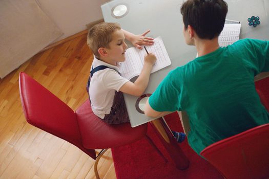 young mom woman doing home work with elementary school grade boy at home in kitchen