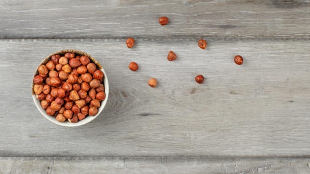 Table top view on small bowl full of hazelnuts on gray wood desk.