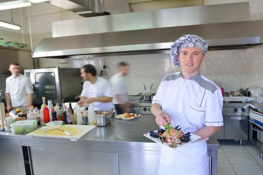 Handsome chef dressed in white uniform decorating pasta salad and seafood fish in modern kitchen