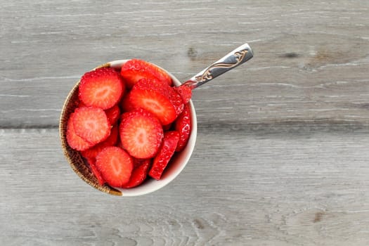 Table top view on small bowl of raspberries cut in small pieces, with silver spoon - ready to eat healthy snack.