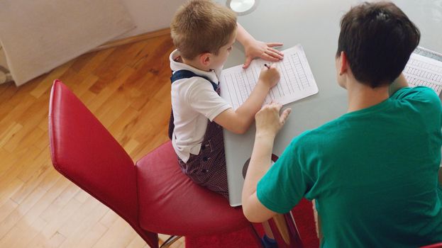 young mom woman doing home work with elementary school grade boy at home in kitchen