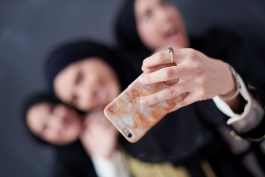 group of young beautiful muslim women in fashionable dress with hijab using mobile phone while taking selfie picture in front of black chalkboard representing modern islam fashion technology and ramadan kareem concept